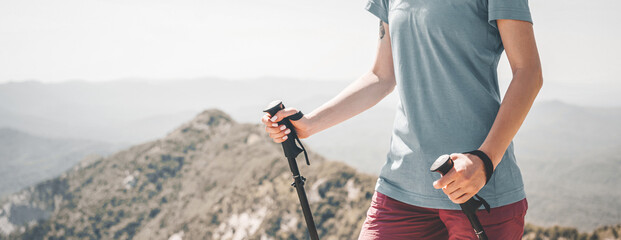 Sporty young woman walking with trekking poles in mountains.