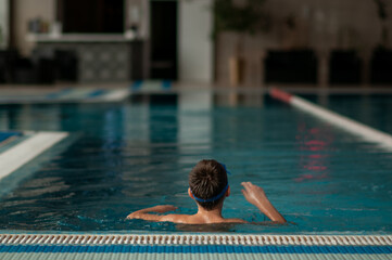 boy swims in the pool standing at the edge of the water