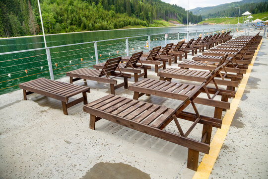 Row of empty wooden beach chairs near water.