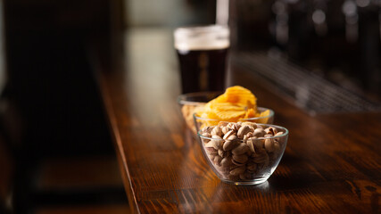 Menu for client. Pistachios, chips, nuts and glass of dark beer with foam on bar counter in interior