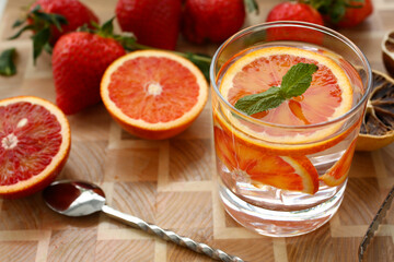 Top view of refreshing drink with orange slice and mint leaf on the wooden table with strawberries on the background