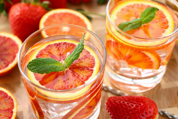 Close up of summer fresh fruit in glass of water on the wooden table with strawberries on the background