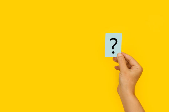 Mano de mujer sosteniendo un papel con el signo de interrogaci&oacute;n sobre el fondo amarillo brillante liso y aislado. Vista de frente. Copy space
