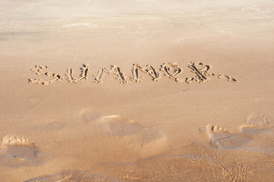 The inscription summer on the sand by the water. Photos on the beach on a Sunny day