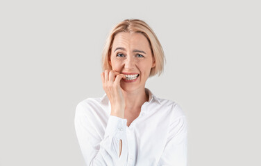 Mature secretary biting her nails in panic against light background