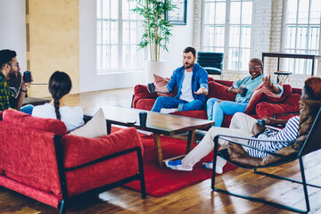 Happy group of male and female colleagues resting in lounge zone of coworking space during work break,young multiracial friends communicating and having fun during free time in modern loft office .