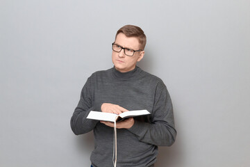Portrait of serious man holding open big book and looking aside