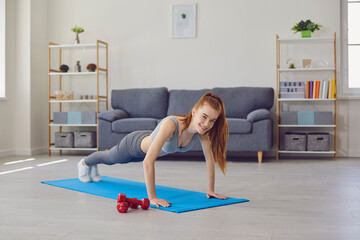 Naklejka premium Home sports. Beautiful girl doing push ups or plank on yoga mat indoors. Fit young woman working out in living room