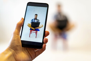 Photo on the phone of a man with a laptop sitting on a chair.