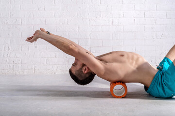 A young man in shorts is doing exercises on a foam roller on his back.