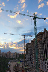 Wide-angle landscape view of construction site with two high town cranes. Construction of the new residential building. Building under construction.Beautiful sun rising sky with fantastic soft clouds