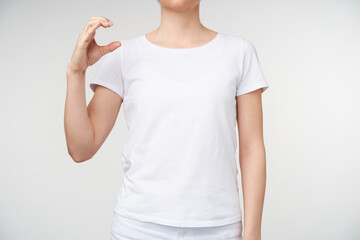 Horizontal shot of young female dressed in casual clothes raising her hand and forming with fingers...