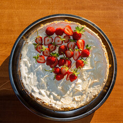 cake with young strawberries in cream is on the table on a sunny day in the open air.