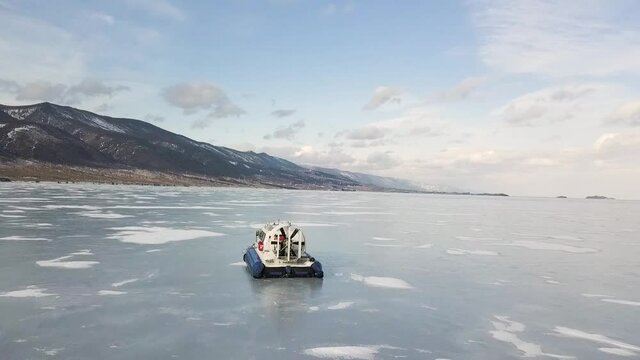 Hovercraft transport on the frozen lake Baikal Siberia, Russia. Clip. Aerial view of picturesque winter landscape with high mountains, frozen lake and blue cloudy sky.
