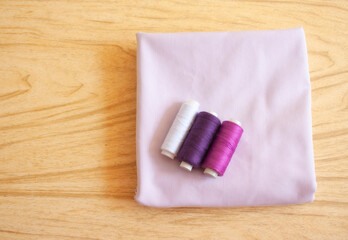 Three spools of thread for sewing (white, purple and pink colors) lie on a fabric on the table, top view.