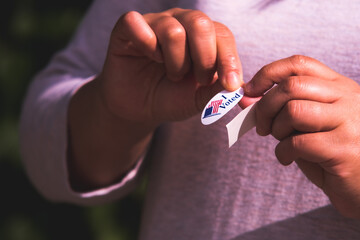 American woman peeling sticker off of backing to place on clothes to communicate to others that she had voted after leaving polling location