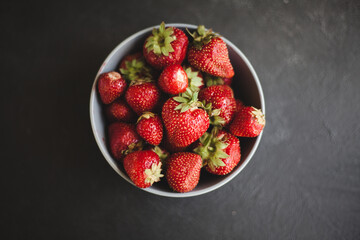 Fresh ripe tasty strawberries in a black plate on a gray wooden background. Flat lay