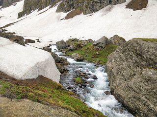 Beautiful river stream flowing in between a huge rock on one side and a snow glacier on other side in an epic Indian Himalayan Valley.