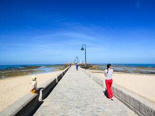 Tourist family mother and son on the walkway to the horizon in the atlantic ocean in time of low tide, Cadiz, Andalusia, Spain