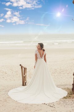 Beautiful bride in her wedding dress posing with her back to photos on the beach.