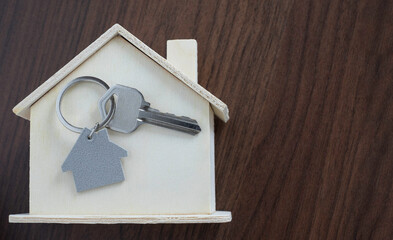 Close-up of Silver key house with house shaped keychain and home mock-up on wooden table background.