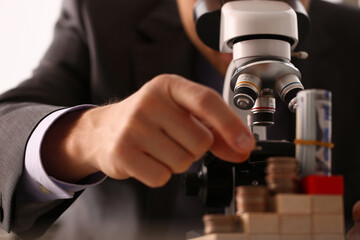 Cropped photo of businessman examining construction of cubes and money through microscope. Trade profit and money concept