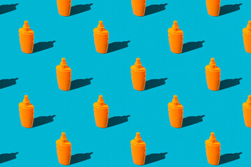 Summer vacation minimal concept. Pattern of orange sunscreen lotion bottles on blue background