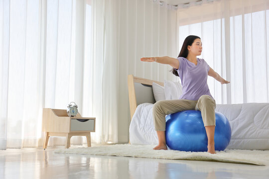 Asian Woman Doing Yoga Exercise With Fitness Ball In Her Bedroom As A Result Of Social Distancing And Quarantine Period With Copy Space