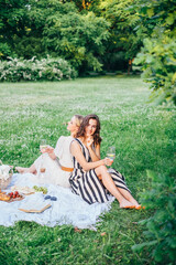 Outdoor countryside portrait of two happy sisters and best friends, enjoying picnic at vintage French style, stylish feminine outfits, tasty food and vine, nice time together. Summer time at nature 