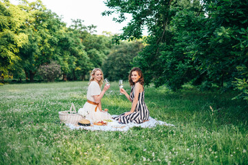 Outdoor countryside portrait of two happy sisters and best friends, enjoying picnic at vintage French style, stylish feminine outfits, tasty food and vine, nice time together. Summer time at nature 
