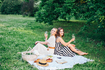 Outdoor countryside portrait of two happy sisters and best friends, enjoying picnic at vintage French style, stylish feminine outfits, tasty food and vine, nice time together. Summer time at nature 