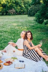 Outdoor countryside portrait of two happy sisters and best friends, enjoying picnic at vintage French style, stylish feminine outfits, tasty food and vine, nice time together. Summer time at nature 