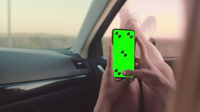 Close-up of a girl's hands holding a phone with a chromakey, a girl sitting in the passenger seat with her legs out the window