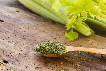 Dried green celery in a wooden spoon and fresh celery on a wooden table