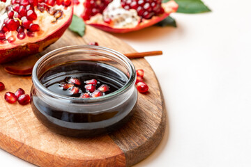 Narsharab (Azerbaijani: Narşərab) -Azerbaijani pomegranate sauce in a glass bowl closeup and fresh pomegranate on a white background. copy space. Fruit sauce for meat, oriental cuisine. Space for text