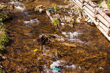 Stream with running water, polluted by plastic garbage