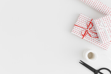 White gifts, twine, scissors and paper roll on a white table. Flat lay with blank copy space.