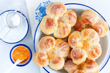 Beautiful yeast buns in the shape of flowers in an enameled bowl, top view, selective focus