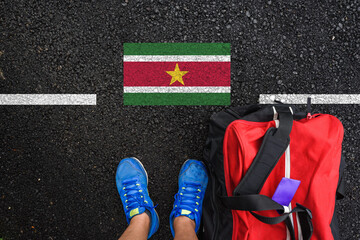 a man with a shoes and travel bag is standing on asphalt next to flag of Suriname and border