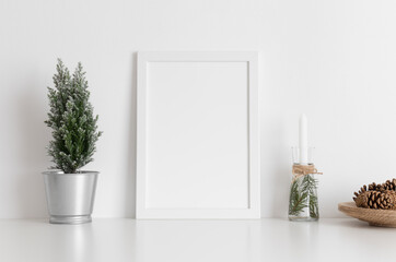 White frame mockup with a cypress tree, candles and pine cones on a white table. Christmas decoration.