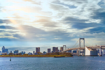 Seascape of the Bird Island of Odaiba Bay in front of the double-layered suspension Rainbow Bridge in the port of Tokyo with altostratus clouds in the sky.