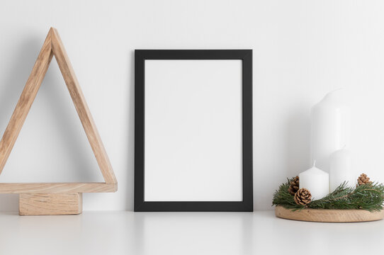 Black frame mockup with a wooden tree and candles on a white table.