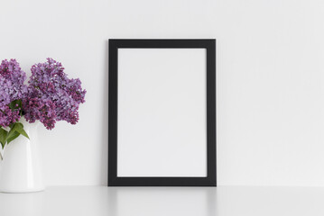 Black frame mockup with a bouquet of lilac in a vase on a white table.Portrait orientation.
