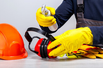 Coronavirus treatment concept. Handyman or builder using disinfectant for sanitizing ear muffs...