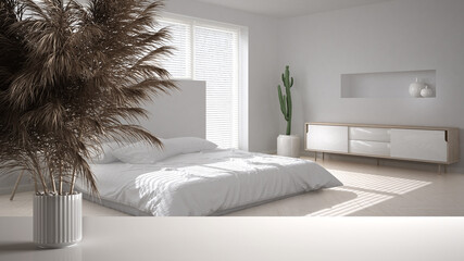 White table top or shelf with straws, dry plants, ornament, ears, sheaf, branch in vase, over minimal white bedroom with double bed, modern minimal interior design