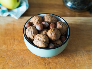 Walnuts and hazelnuts in green bowl on wooden board.