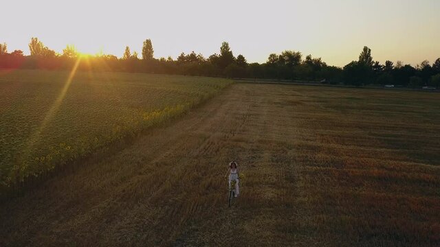 Top view of a woman in a white dress leading a bicycle on a field with sunflowers. Drone futage 4K.