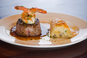 Surf ‘n Turf, lobster tail and steak entree. Filet mignon topped with chanterelle mushrooms & Maine lobster tail topped w/ drawn butter served on white dinner plate. Classic steakhouse menu favorite.