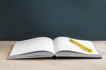 An open book with white lined pages and a yellow pencil, against the school blackboard. Back to the school concept, close-up, copy space