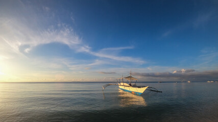 Obraz premium fishing boat on the surface of the sea in calm at sunset